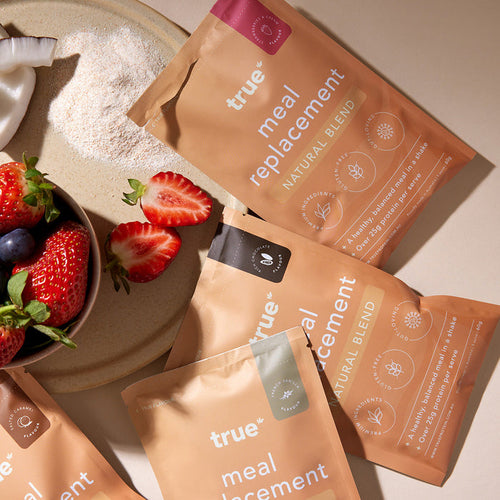 True meal replacement natural blend sample sachets arranged with fresh strawberries, powdered shake mix and bowl — protein shake meal replacement packets for healthy weight management and on-the-go nutrition.