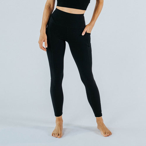 Women's high-waist black full-length active leggings with side phone pockets, fitted athleisure yoga workout pants on model against clean white studio background.