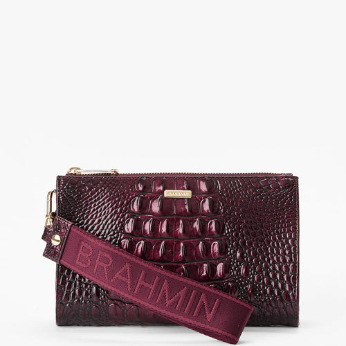 A dark burgundy crocodile-embossed leather clutch bag with a matching fabric shoulder strap embossed with the brand name 'BRAHMIN'. The bag features a gold-tone metal logo plate and zipper pullers, set against a plain white background.