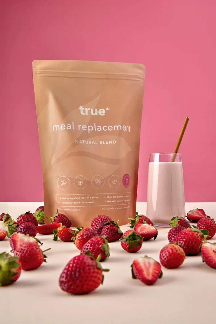True Protein meal replacement natural blend — strawberries & cream flavour pouch with glass of strawberry shake and fresh strawberries on pink background, Australian-made.
