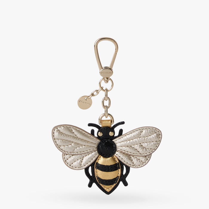 A bee-shaped keychain charm with textured white wings, a black and gold striped body, and a gold-tone clasp on a light gray background.