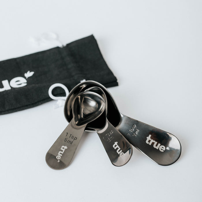 True-branded stainless steel measuring spoon set (1 tsp/5 ml, 1 tbsp/15 ml, 2 tsp/10 ml) with black drawstring pouch on white background