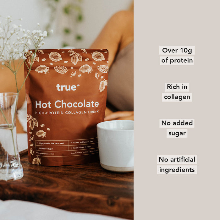 True Hot Chocolate high-protein collagen drink pouch on wooden table next to white mug and glass, promoting over 10g protein, rich in collagen, no added sugar and no artificial ingredients — proudly made in Australia.