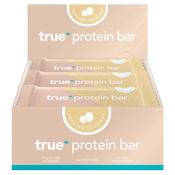 Box of 12 True Protein Bar toasted coconut flavor in peach-beige display packaging, 63g serving size, 14.3g protein per bar — protein snack bar retail box, healthy vegan-friendly snack (front view)