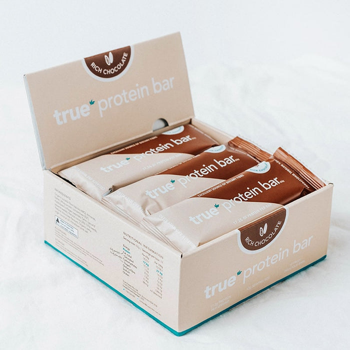 Open retail box of True Protein Bar — Rich Chocolate flavor, individually wrapped protein bars arranged inside on a white background.