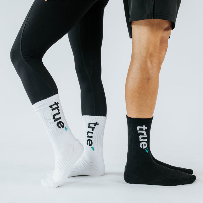 White and black crew athletic socks with "true" logo worn by male and female models on white studio background — unisex performance cotton-blend socks for running and gym.