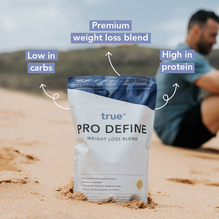 True Pro Define weight loss blend pouch standing in sand on a beach, labelled low in carbs and high in protein, premium weight-loss protein powder for dieting and fitness.