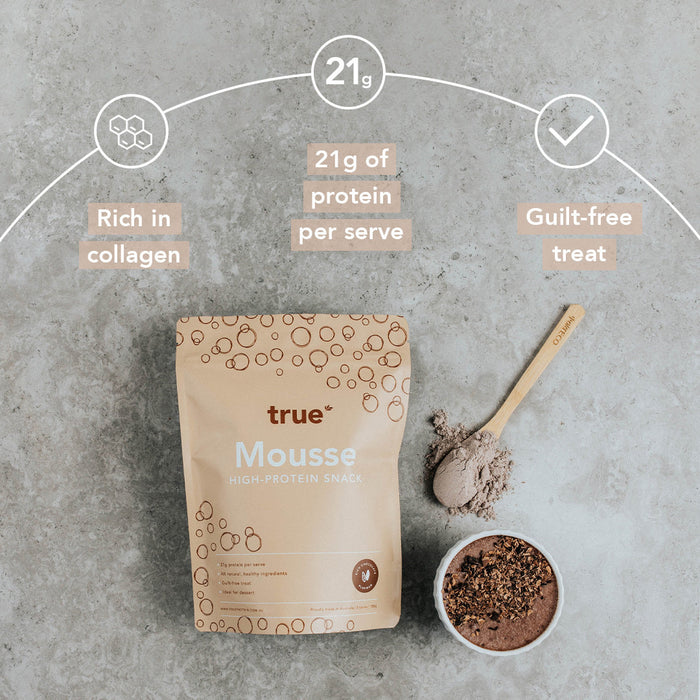 True Mousse high-protein snack pouch on a concrete surface with a wooden scoop of chocolate powder and a prepared chocolate mousse bowl; packaging highlights “21g of protein per serve,” “rich in collagen” and “guilt-free treat.”