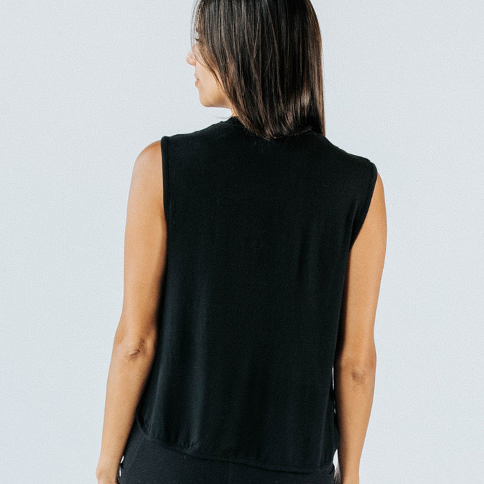 Back view of a woman wearing a black sleeveless crop top — women's casual athleisure top on model, studio white background, product fashion photography.